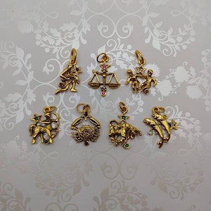 May include: A set of 8 gold-toned zodiac charms with colorful gemstones. The charms feature the astrological signs of Sagittarius, Cancer, Taurus, Pisces, Gemini, Libra, Virgo, and Capricorn.