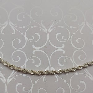 May include: A silver rope chain necklace. The chain is made of small, linked, twisted silver pieces.