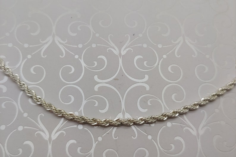May include: A silver rope chain necklace. The chain is made of small, linked, twisted silver pieces.