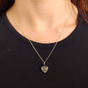 May include: A silver chain necklace with a clear heart-shaped pendant containing a small gold bead.