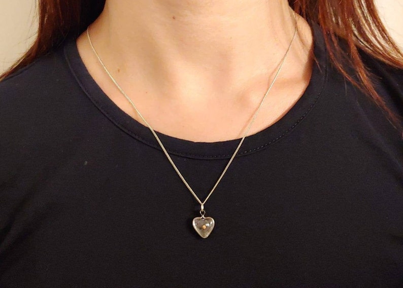 May include: A silver chain necklace with a clear heart-shaped pendant containing a small gold bead.