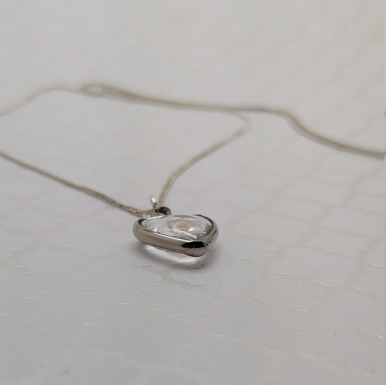 May include: A silver chain necklace with a heart-shaped pendant. The pendant is clear and contains a small, white flower inside.