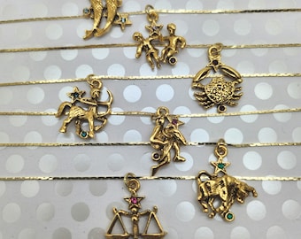 May include: A set of 12 gold zodiac charms with colorful gemstones. Each charm features a different zodiac sign, including Aries, Taurus, Gemini, Cancer, Leo, Virgo, Libra, Scorpio, Sagittarius, Capricorn, Aquarius, and Pisces.