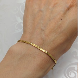 May include: A gold chain bracelet with a square link design. The bracelet is on a person's wrist.