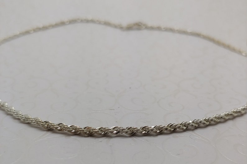 May include: A silver rope chain necklace. The chain is made of small, twisted links.