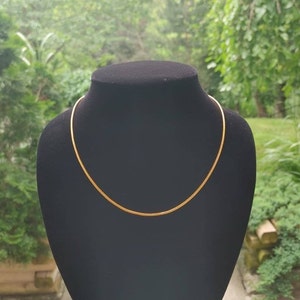 May include: A gold chain necklace displayed on a black stand. The chain is thin and has a smooth, shiny finish.