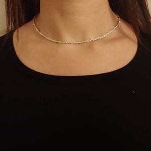 May include: A silver rope chain necklace on a person wearing a black shirt.