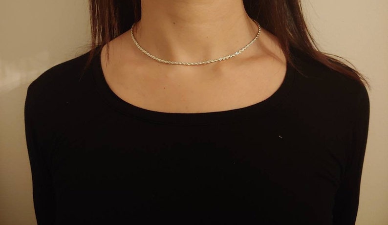May include: A silver rope chain necklace on a person wearing a black shirt.