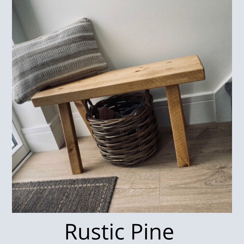 Puede incluir: Banco de pino r&uacute;stico con asiento rectangular y cuatro patas robustas. Una cesta de mimbre se encuentra debajo del banco, y un coj&iacute;n a rayas descansa contra la pared. El texto "Rustic Pine" se muestra en la parte inferior.