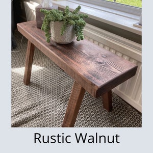Puede incluir: Un banco de madera r&uacute;stico te&ntilde;ido de nogal con patas anguladas. El banco tiene una parte superior rectangular y se exhibe en interiores. Una maceta blanca estampada con una planta verde se encuentra en el banco. El texto "Rustic Walnut" est&aacute; en la parte inferior.