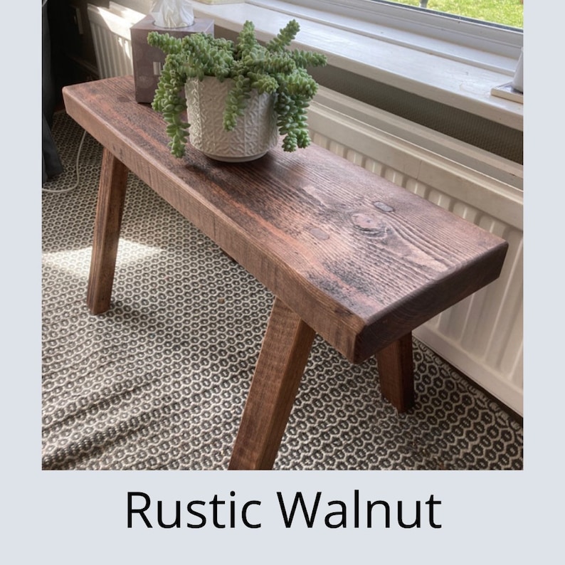 Puede incluir: Un banco de madera r&uacute;stico te&ntilde;ido de nogal con patas anguladas. El banco tiene una parte superior rectangular y se exhibe en interiores. Una maceta blanca estampada con una planta verde se encuentra en el banco. El texto "Rustic Walnut" est&aacute; en la parte inferior.