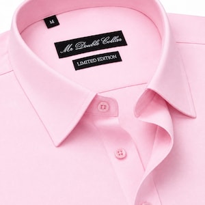 Może przedstawiać: Jasnoróżowa koszula zapinana na guziki ze spiczastym kołnierzykiem. Wewnętrzna metka na karku zawiera napis Mr Double Collar oraz LIMITED EDITION, a osobna mała czarna metka wskazuje rozmiar M. Koszula posiada pasujące różowe guziki z przodu.
