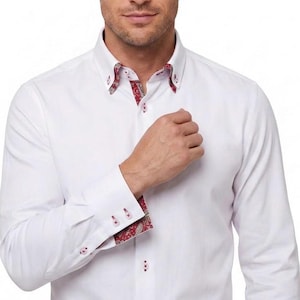 May include: A crisp white long-sleeve button-down shirt featuring a button-down collar with a red and white paisley pattern on the inner collar lining and inner cuffs. The shirt includes white buttons with red stitching details on the front placket.