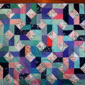 May include: A colorful quilt with a geometric pattern of triangles in shades of blue, green, pink, and purple. The quilt is made of various fabrics with different patterns and textures.