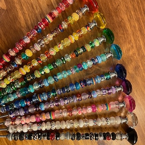 May include: A set of 14 colorful beaded wands with crystal tops. Each wand features a different color scheme and bead pattern, including rainbow, black and white, and pink and purple.