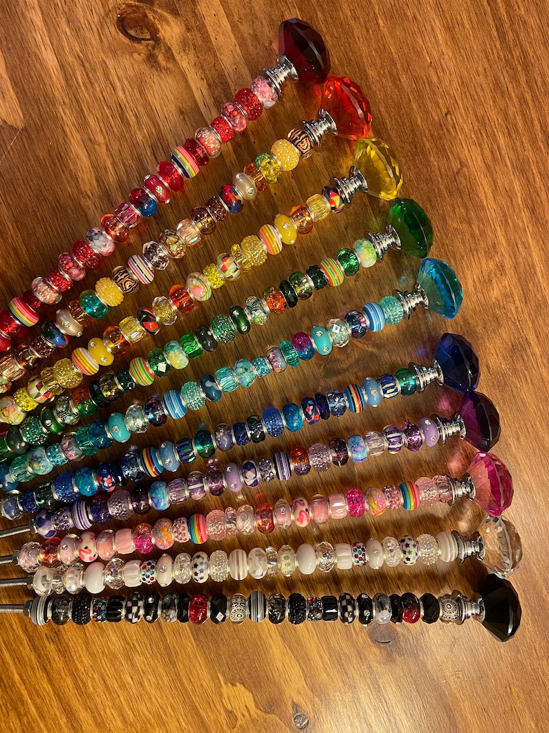 May include: A set of 14 colorful beaded wands with crystal tops. Each wand features a different color scheme and bead pattern, including rainbow, black and white, and pink and purple.
