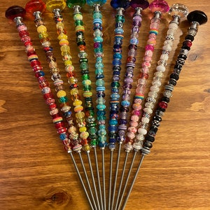 May include: A set of 12 colorful beaded wands with crystal tops. Each wand features a different color scheme and pattern of beads. The wands are made of metal and have a silver finish.