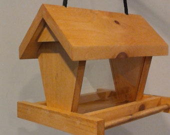 Peut inclure: Mangeoire à oiseaux en bois avec un toit en pente et un plateau. La mangeoire est faite de bois de couleur claire et a un design simple et fonctionnel. Une corde noire est attachée pour la suspension. Conçu pour attirer les oiseaux.