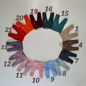 May include: A circular arrangement of small trousers in various colours, including orange, red, purple, pink, blue, and brown. Each pair features a drawstring waist, side pockets, and numbered labels from 1 to 21, showcasing a diverse colour palette.