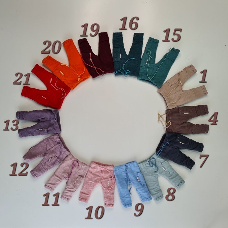 May include: A circular arrangement of small trousers in various colours, including orange, red, purple, pink, blue, and brown. Each pair features a drawstring waist, side pockets, and numbered labels from 1 to 21, showcasing a diverse colour palette.