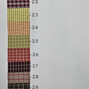 May include: A vertical fabric swatch chart featuring eight distinct plaid and checkered patterns labeled with numbers 22 through 29. The colors include maroon, yellow, orange, olive green, rust red, dark brown, beige, and charcoal gray with white lines.