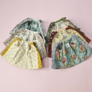 May include: A collection of six small, flared skirts featuring various floral patterns in shades of yellow, blue, green, and brown. Each skirt has a visible white interior label with the text A.W. printed in black, and a textured fabric finish.