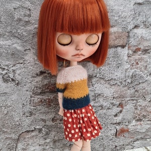May include: A doll with red hair wearing a yellow, blue, and white striped sweater and a red and white polka dot skirt.