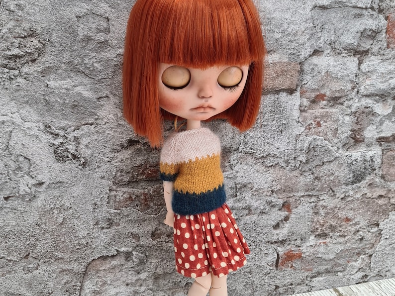May include: A doll with red hair wearing a yellow, blue, and white striped sweater and a red and white polka dot skirt.