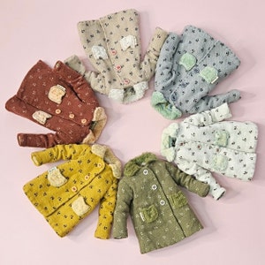 May include: Six miniature coats arranged in a circle, each featuring a small floral pattern, a fuzzy collar, two front pockets, and button closures. The coats come in various colors including beige, blue, rust, yellow, green, and off-white.