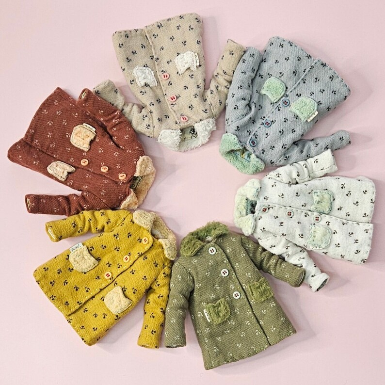 May include: Six miniature coats arranged in a circle, each featuring a small floral pattern, a fuzzy collar, two front pockets, and button closures. The coats come in various colors including beige, blue, rust, yellow, green, and off-white.