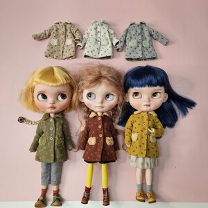 May include: Three dolls with distinct hair colors&mdash;blonde, light brown, and dark blue&mdash;each wearing a patterned coat with two pockets and buttons. Above them are three additional miniature coats in beige, white, and gray, all featuring matching patterns.