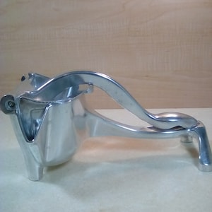 May include: A silver metal citrus juicer with a lever handle. The juicer has a base with three legs and a spout for pouring juice.