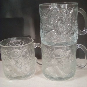 May include: Four clear glass mugs with a raised design of Batman and the Joker. The mugs have a handle on the right side.