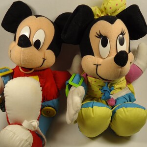 May include: A pair of plush Mickey Mouse and Minnie Mouse toys. Mickey is wearing a red, blue, and yellow outfit. Minnie is wearing a yellow, blue, and pink outfit with white polka dots.