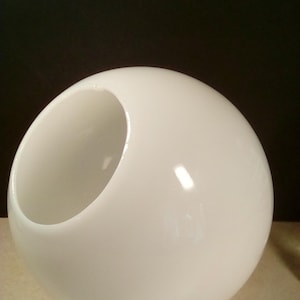May include: A glossy white spherical decorative bowl with a large opening on one side. The bowl has a smooth, reflective surface and a modern, minimalist design. The background is a dark color.