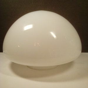 May include: A white, dome-shaped glass light fixture. The fixture has a rounded top and a circular base. The surface is smooth and reflects light, creating highlights. The overall shape resembles a mushroom. The background is dark.
