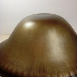 May include: A large, bronze-colored bowl with a wide, fluted rim. The bowl has a smooth, reflective surface with a dark brown gradient towards the rim. The bowl's shape is reminiscent of a bell or a shallow dome.