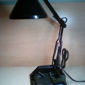 May include: A black desk lamp with a flexible arm and a black shade. The lamp has a built-in organizer with compartments for pens, pencils, and other office supplies. The organizer also has a clip for holding papers.