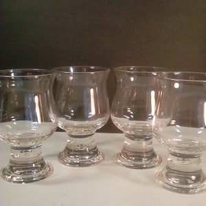 May include: Set of four clear glass stemmed drinking glasses with a rounded bowl and a thick base.