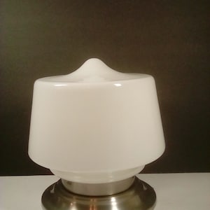 May include: A white glass lamp shade with a rounded top and a flared, conical shape. It sits atop a brushed metal base. The lamp has a classic, minimalist design.