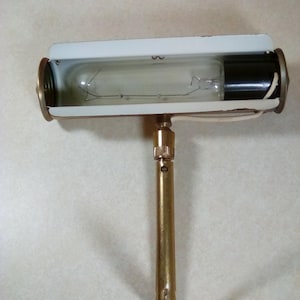 May include: A brass wall-mounted reading lamp with a white shade and a clear light bulb. The lamp has a long, adjustable arm.