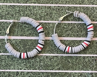 May include: A pair of large hoop earrings made of gray and white polymer clay beads with red accents. The earrings are on a green and white background.