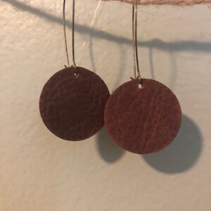 May include: A pair of brown leather earrings with a circular shape and a simple gold hook.