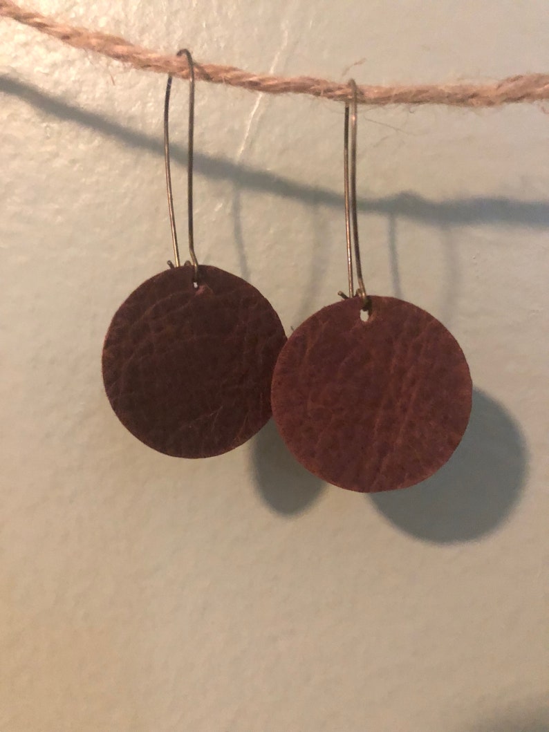 May include: A pair of brown leather earrings with a circular shape and a simple gold hook.