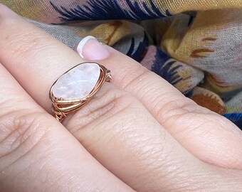 May include: A ring with a white oval-shaped gemstone wrapped in copper wire.