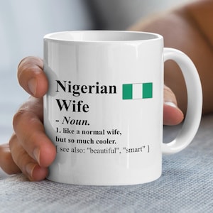 May include: A white ceramic mug featuring the black printed text: Nigerian Wife - Noun. 1. like a normal wife, but so much cooler. [ see also: "beautiful", "smart" ] and a small rectangular green and white Nigerian flag icon.