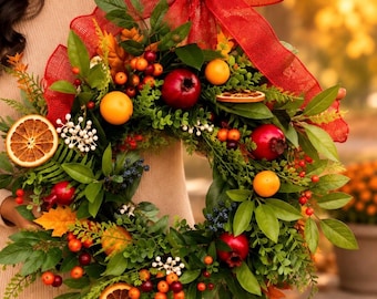 May include: A decorative wreath featuring green foliage, red pomegranates, orange citrus slices, and small berries. The circular arrangement is accented with a large, textured red burlap bow at the top, creating a seasonal display of natural elements.