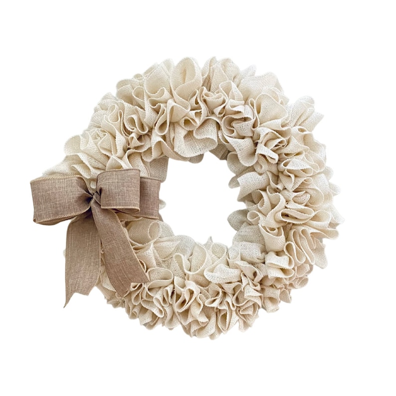 May include: A cream-colored burlap wreath with a brown burlap bow. The wreath is made of fabric and has a ruffled texture.