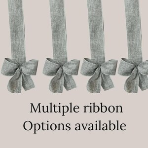 May include: Four gray fabric ribbons with bow details. The ribbons are hanging against a light beige background. The text "Multiple ribbon Options available" is displayed in black font.