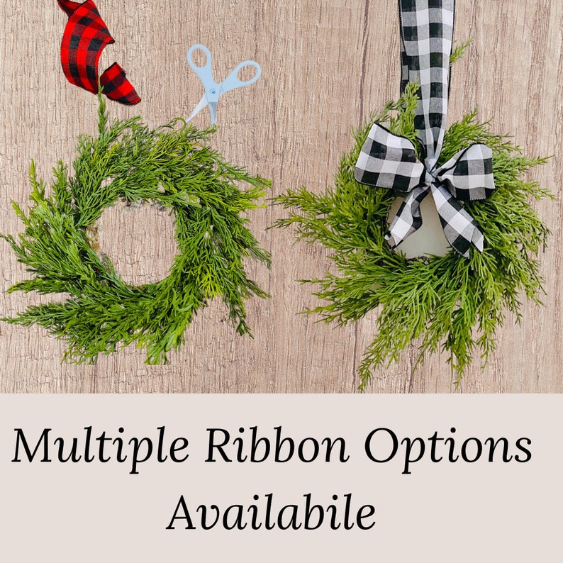 Op de afbeelding: Twee kleine groene kransen met verschillende lint opties. E&eacute;n krans heeft een zwart-wit geruit lint gebonden in een strik. De andere krans heeft een rood-zwart geruit lint. De tekst "Multiple Ribbon Options Available" staat onderaan de afbeelding.